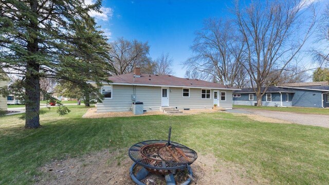 rear view of house with a lawn, a fire pit, and entry steps