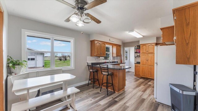 kitchen featuring dark countertops, a kitchen breakfast bar, light wood-style flooring, freestanding refrigerator, and a peninsula