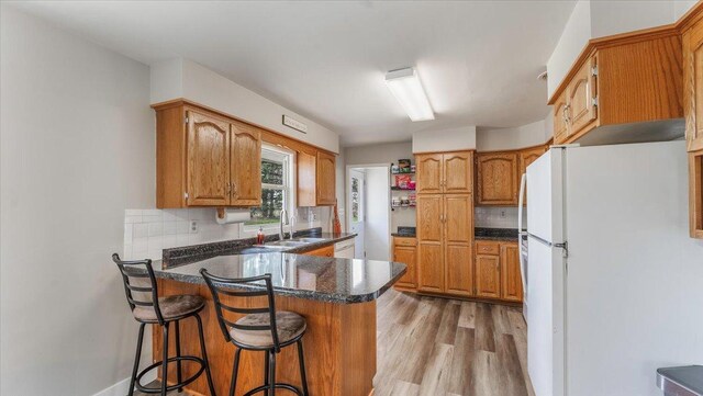 kitchen featuring dark countertops, a sink, a peninsula, light wood finished floors, and white appliances