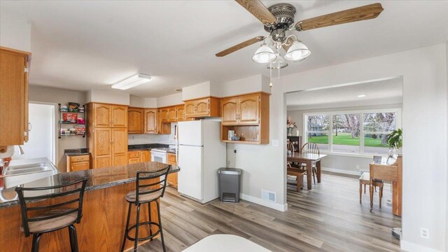 kitchen with a ceiling fan, visible vents, a sink, a peninsula, and white appliances
