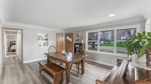 dining space with baseboards, light wood-style flooring, a textured ceiling, and visible vents
