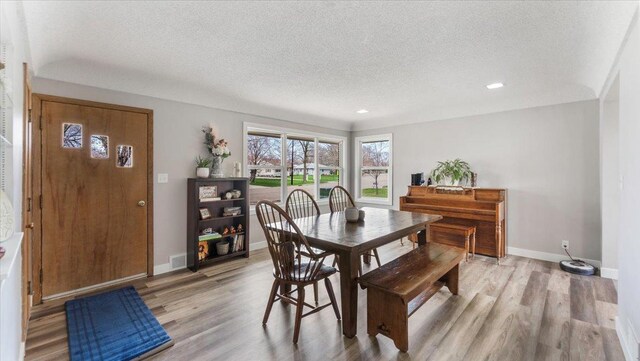 dining space with baseboards, light wood-type flooring, a textured ceiling, and visible vents