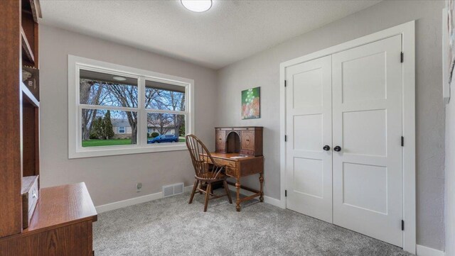 carpeted home office featuring baseboards, a textured ceiling, and visible vents