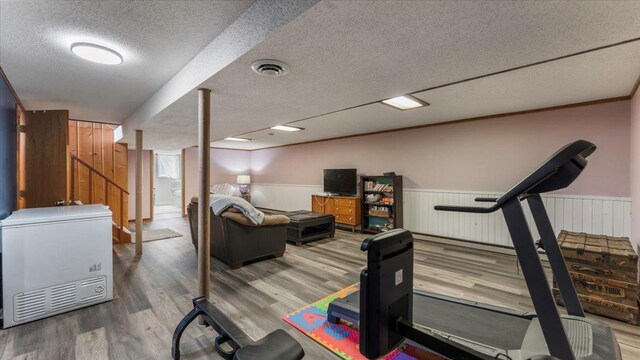 workout room featuring a wainscoted wall, visible vents, a textured ceiling, and wood finished floors