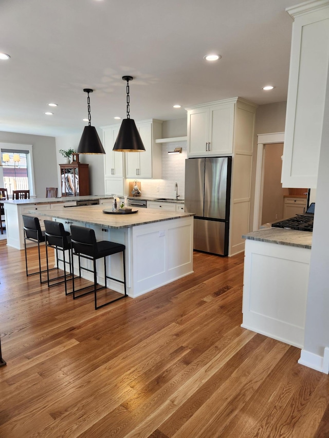 kitchen featuring freestanding refrigerator, a sink, white cabinets, tasteful backsplash, and light wood finished floors