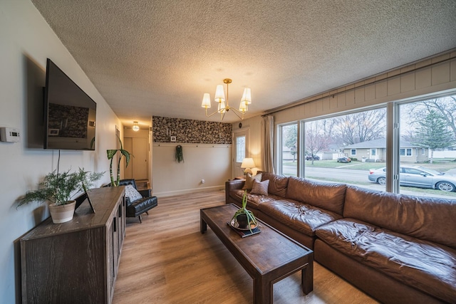 living area with an inviting chandelier, a textured ceiling, light wood-style floors, and baseboards