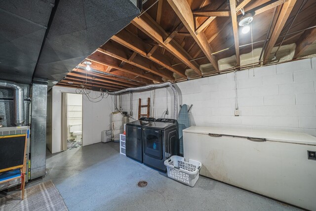 unfinished below grade area featuring washing machine and clothes dryer, concrete block wall, heating unit, and water heater