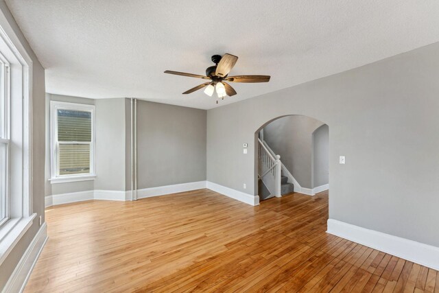 spare room featuring stairs, ceiling fan, a textured ceiling, arched walkways, and light wood-style flooring