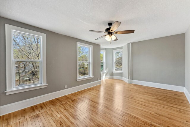 spare room with light wood-style floors, baseboards, a ceiling fan, and a textured ceiling