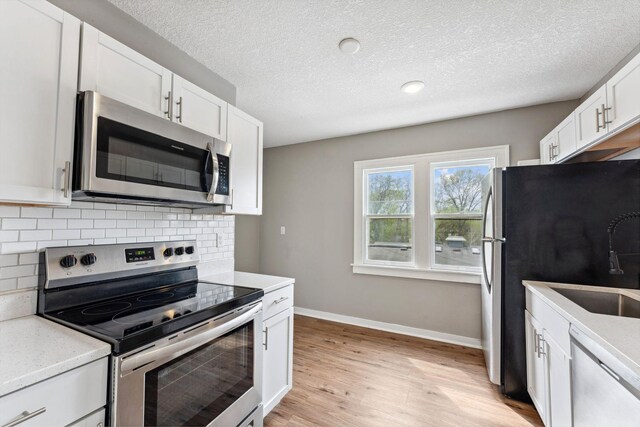 kitchen featuring baseboards, decorative backsplash, white cabinetry, and appliances with stainless steel finishes
