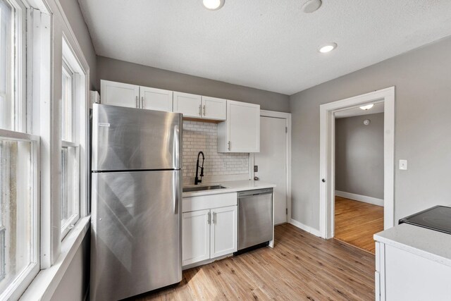 kitchen with white cabinets, tasteful backsplash, a sink, light wood-style flooring, and appliances with stainless steel finishes