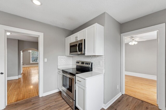 kitchen with arched walkways, light wood-type flooring, light countertops, white cabinets, and stainless steel appliances