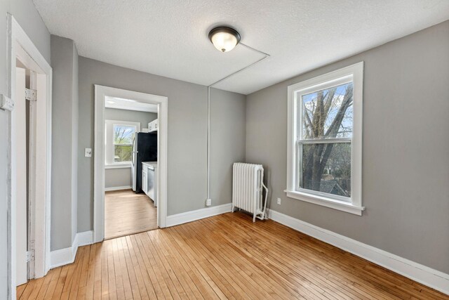 unfurnished room with radiator, baseboards, light wood-type flooring, and a textured ceiling