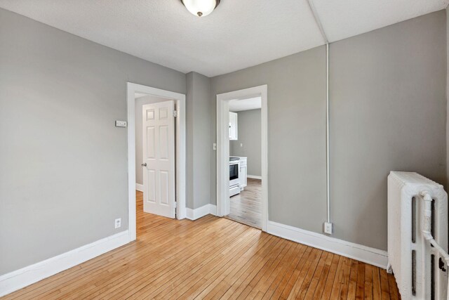 unfurnished bedroom with baseboards, light wood finished floors, and radiator