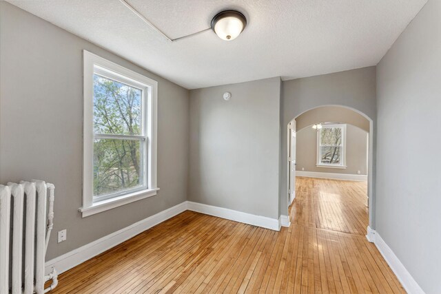 empty room with light wood-style floors, radiator, arched walkways, and a wealth of natural light
