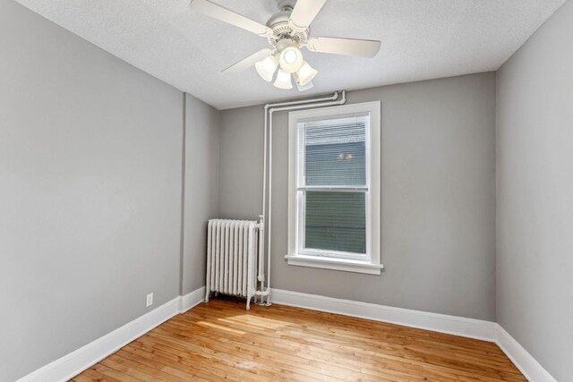 spare room featuring radiator, baseboards, ceiling fan, light wood-type flooring, and a textured ceiling