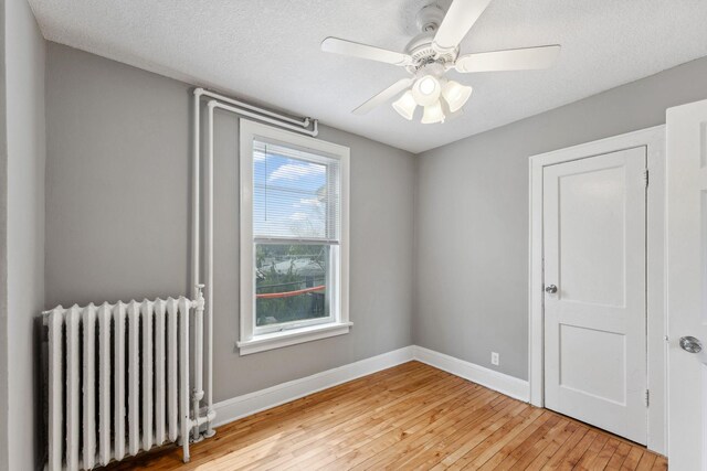 empty room featuring baseboards, ceiling fan, radiator heating unit, a textured ceiling, and light wood-style flooring