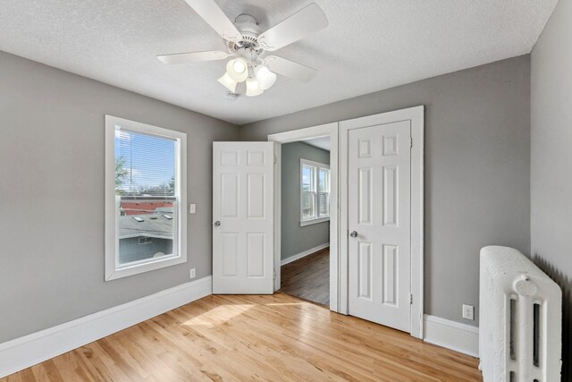 unfurnished bedroom featuring baseboards, multiple windows, radiator heating unit, and light wood-style flooring