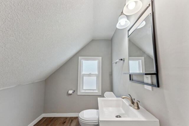 half bathroom with a textured ceiling, a sink, lofted ceiling, and wood finished floors
