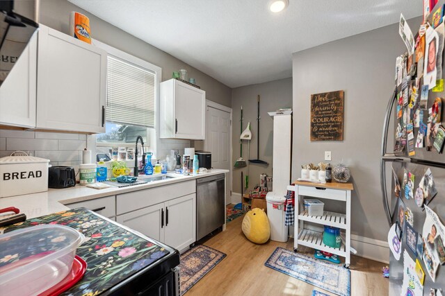 kitchen featuring a sink, appliances with stainless steel finishes, white cabinets, and light wood-style flooring