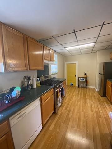 528 Broadway St, Spring Valley, MN 55975 - kitchen featuring brown cabinets, light wood-type flooring, under cabinet range hood, dark countertops, and appliances with stainless steel finishes