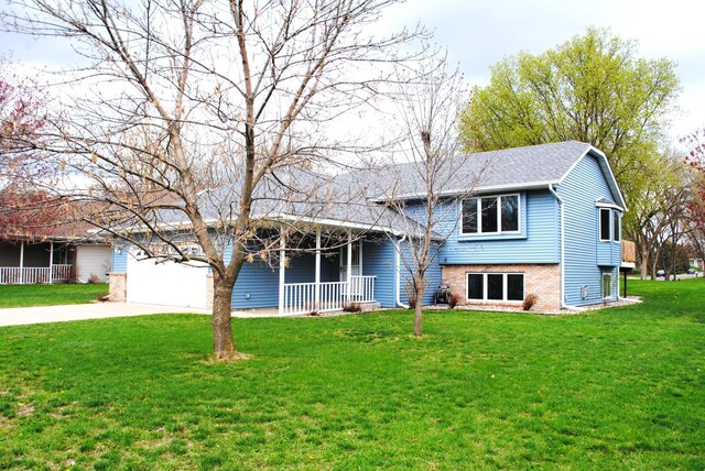 split level home featuring roof with shingles, brick siding, a porch, a front yard, and driveway