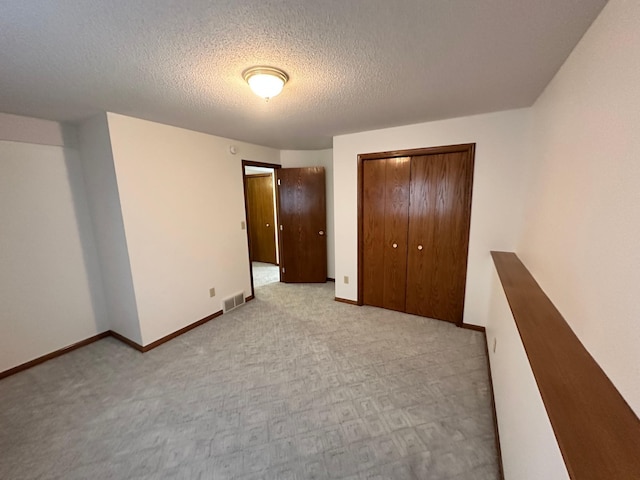 unfurnished bedroom with a textured ceiling, visible vents, baseboards, a closet, and carpet