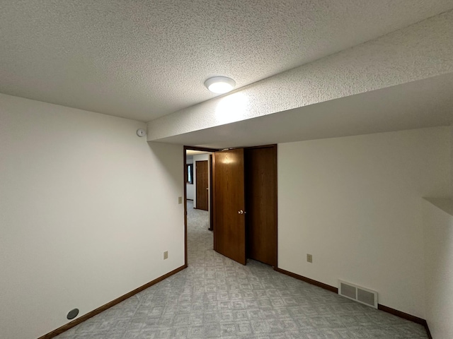 finished below grade area with visible vents, a textured ceiling, baseboards, and light carpet