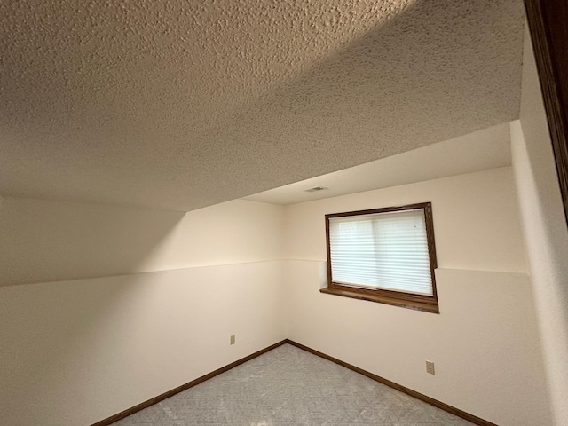 additional living space featuring a textured ceiling, baseboards, and carpet