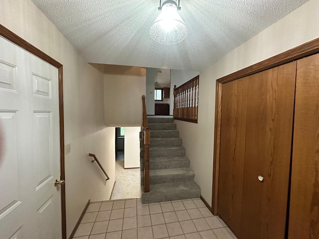 staircase with carpet flooring, a textured ceiling, baseboards, and tile patterned flooring