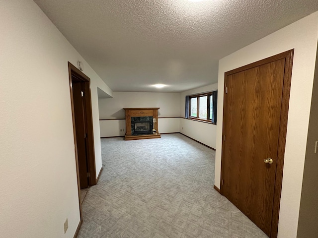 unfurnished living room with light colored carpet, a fireplace with raised hearth, baseboards, and a textured ceiling