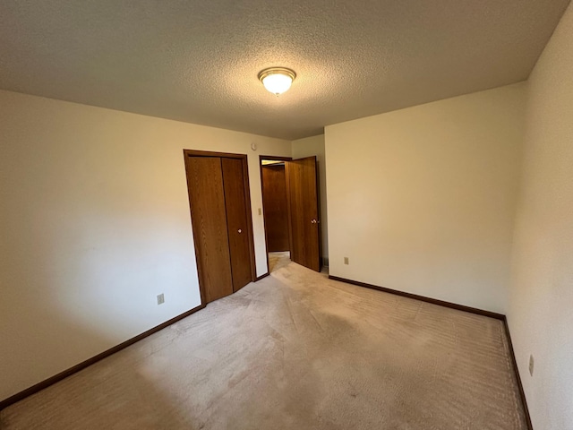 unfurnished bedroom featuring multiple closets, a textured ceiling, baseboards, and light colored carpet