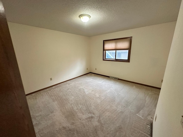 carpeted spare room with a textured ceiling, visible vents, and baseboards