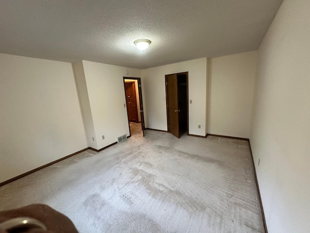 empty room featuring baseboards, light carpet, a textured ceiling, and visible vents