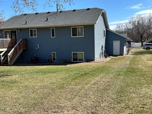 rear view of property featuring a lawn, central AC unit, a shingled roof, and a deck
