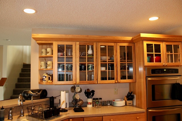 kitchen with light countertops, a textured ceiling, glass insert cabinets, and double oven