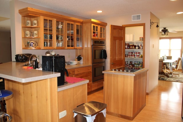 kitchen with black electric stovetop, light wood-style floors, double oven, a peninsula, and visible vents