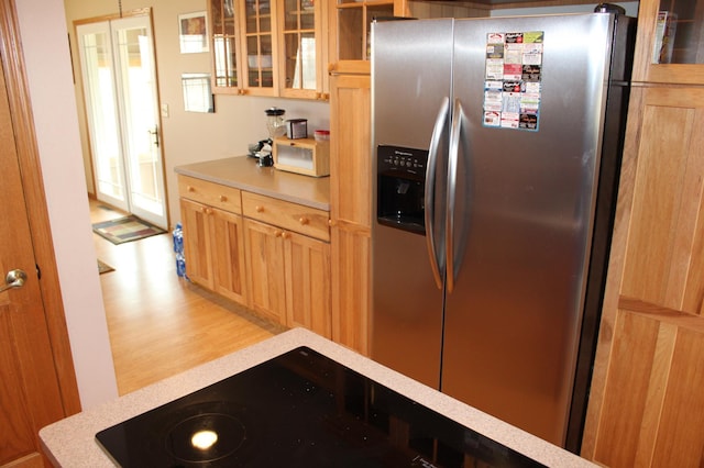kitchen featuring light brown cabinetry, glass insert cabinets, stainless steel fridge, light countertops, and light wood-type flooring