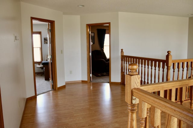 hallway with baseboards, an upstairs landing, and wood finished floors