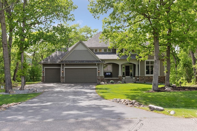 craftsman-style house featuring asphalt driveway, stone siding, an attached garage, and a front yard