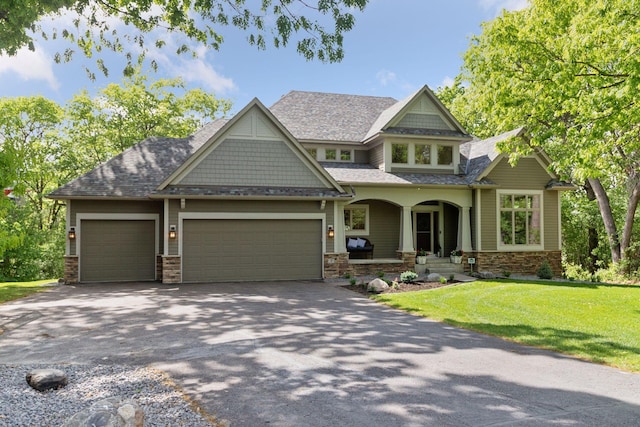 craftsman-style home with a garage, a front lawn, driveway, a porch, and stone siding