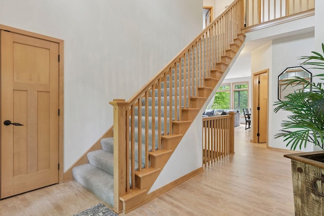 stairway with wood finished floors, a high ceiling, and baseboards