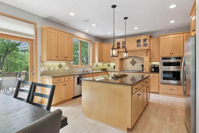 kitchen featuring stainless steel appliances, light brown cabinets, a kitchen island, light wood-style floors, and a sink