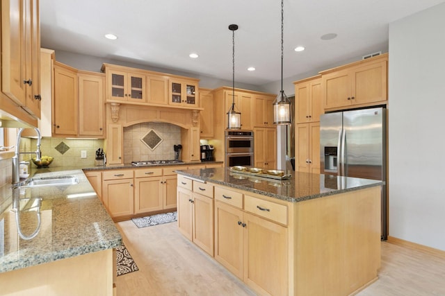kitchen with light brown cabinets, a kitchen island, stainless steel appliances, a sink, and backsplash