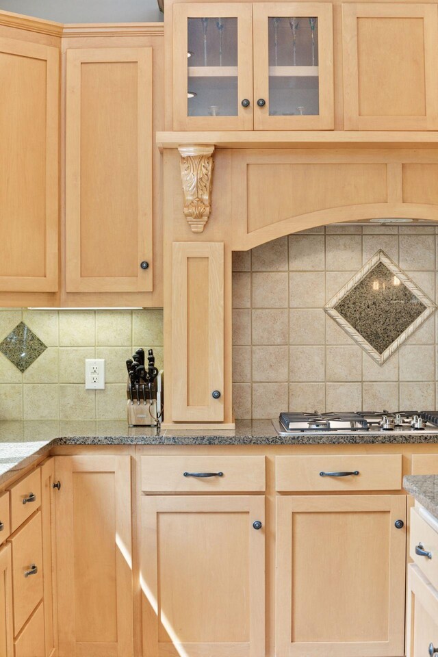 kitchen with light brown cabinets, decorative backsplash, stainless steel gas cooktop, and glass insert cabinets