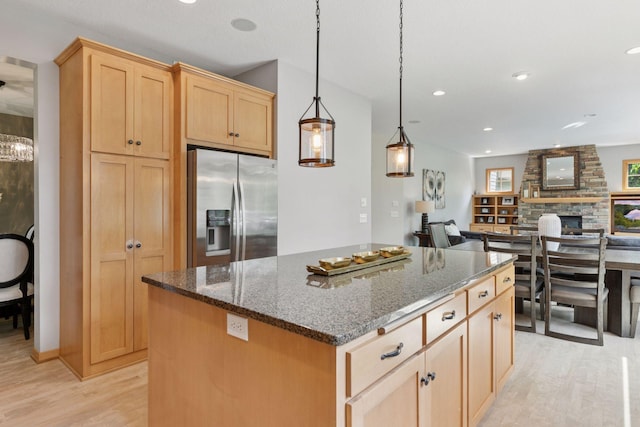 kitchen with stainless steel fridge, light wood-style floors, light brown cabinetry, dark stone countertops, and a center island