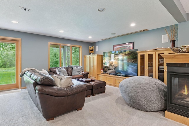 living room with light colored carpet, a glass covered fireplace, healthy amount of natural light, recessed lighting, and a textured ceiling