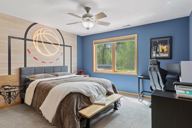 carpeted bedroom with wooden walls, baseboards, ceiling fan, and an office area