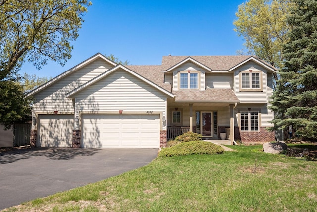 traditional-style house with driveway, brick siding, covered porch, a garage, and a front yard
