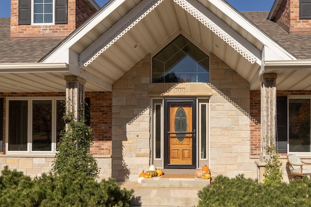view of exterior entry featuring stone siding, brick siding, and roof with shingles